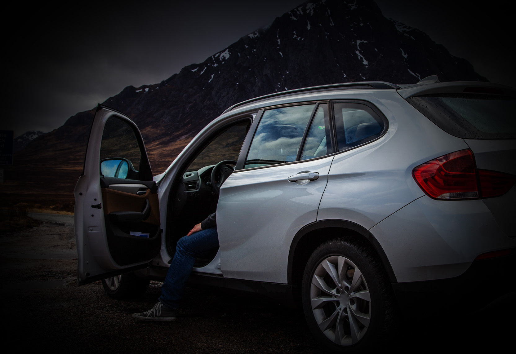 Car parked in the mountains with door open and leg of a person sticking out of door