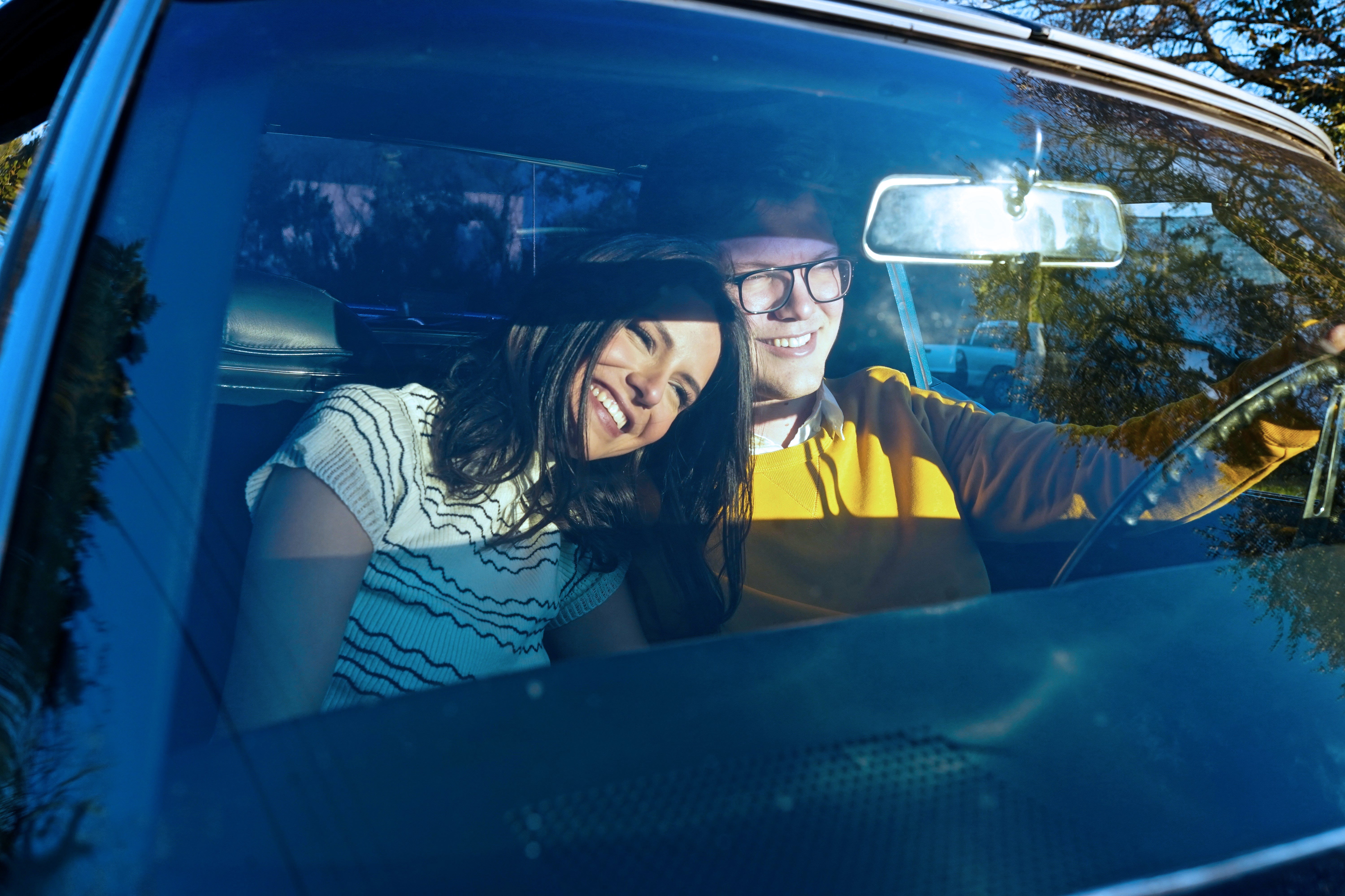 two people driving in car, girl laying on mans shoulder