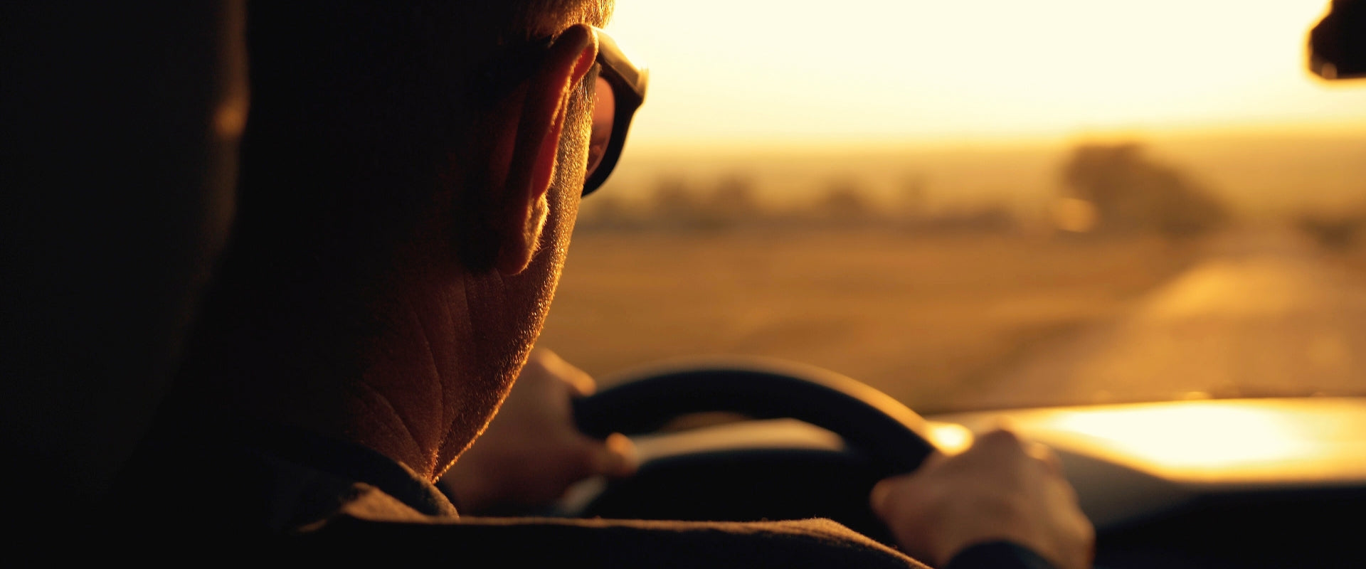 view behind man as he drives and has hands on steering wheel