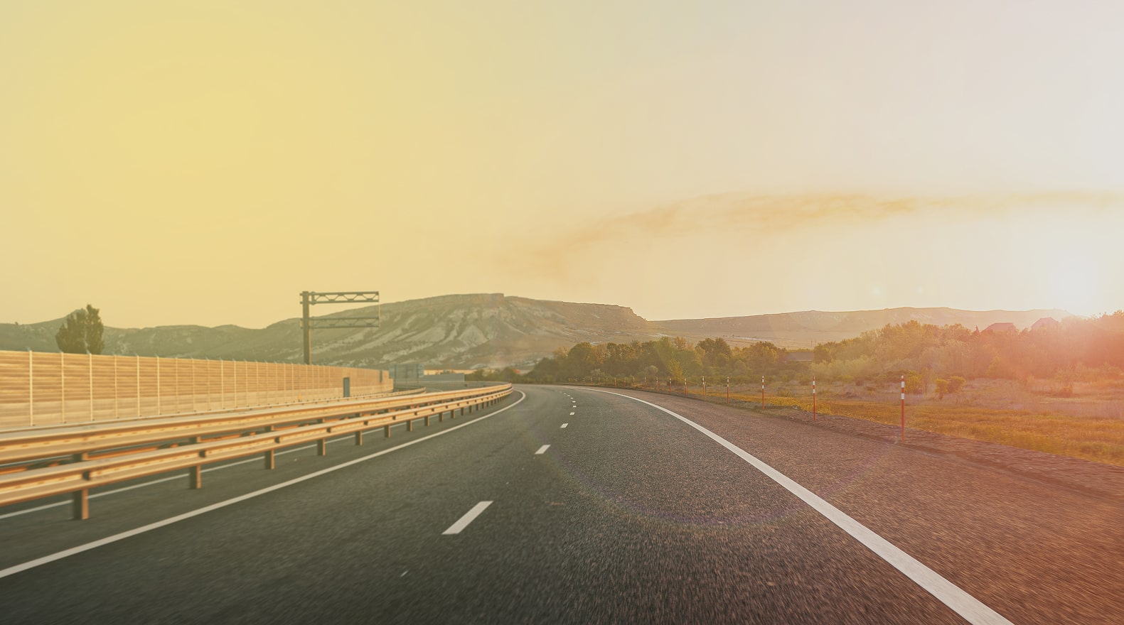 Long stretch of empty road with a scenic view of hills and trees under a warm, sunset sky.